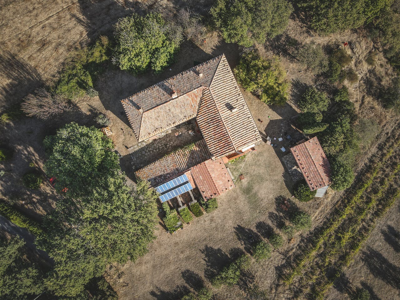 Aerial shot of a rustic farmhouse surrounded by greenery in a rural setting.
