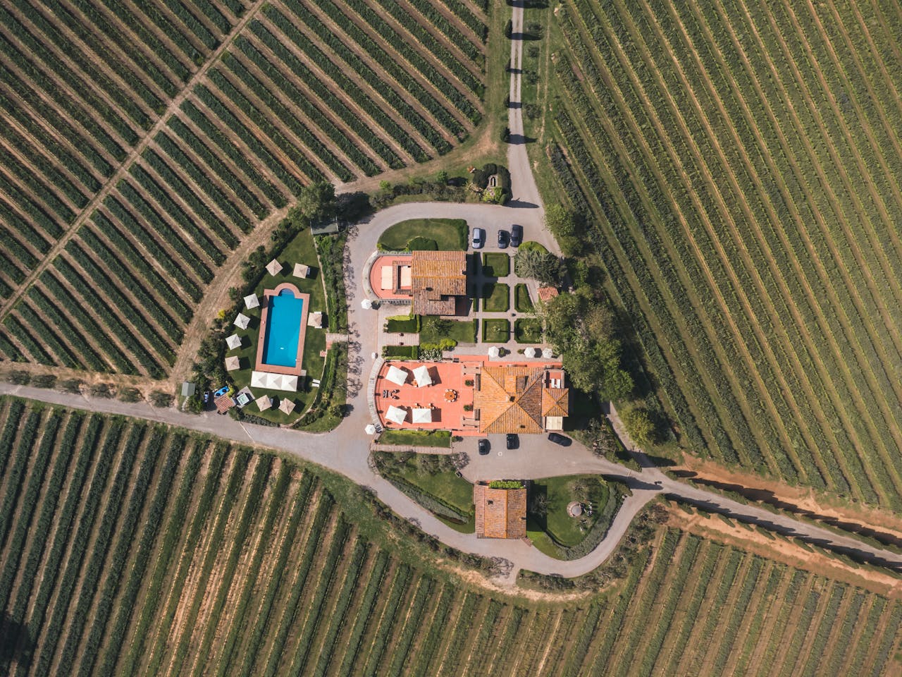 A stunning aerial shot of a traditional farmhouse with a pool and vineyards in Tuscany, Italy.